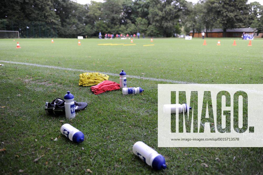 VDV-Trainingscamp --- Fussball --- 1.Bundesliga --- 09.07.2012 Flaschen, Schuhe und Leibchen der VDV, im Hintergrund die Mannschaft beim Training, allgemein, Feature, Hintergrund, Hinterleger