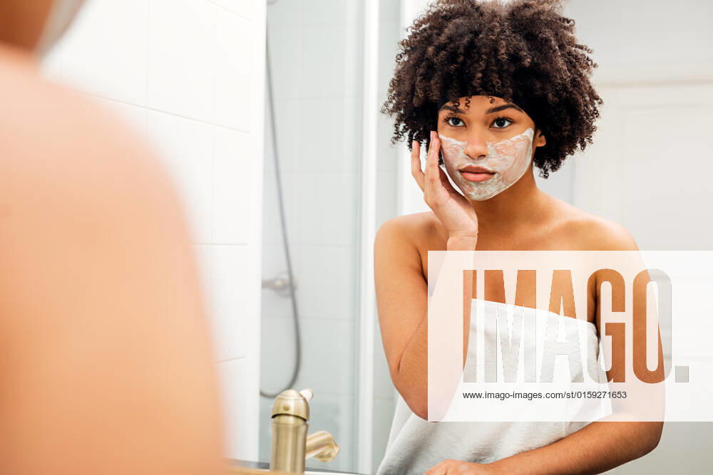 Woman applying facial mask in front of bathroom mirror
