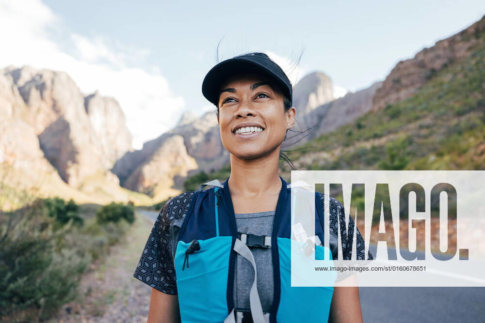 Portrait of a beautiful female hiker in cap. Woman in hiking attire staning in valley.