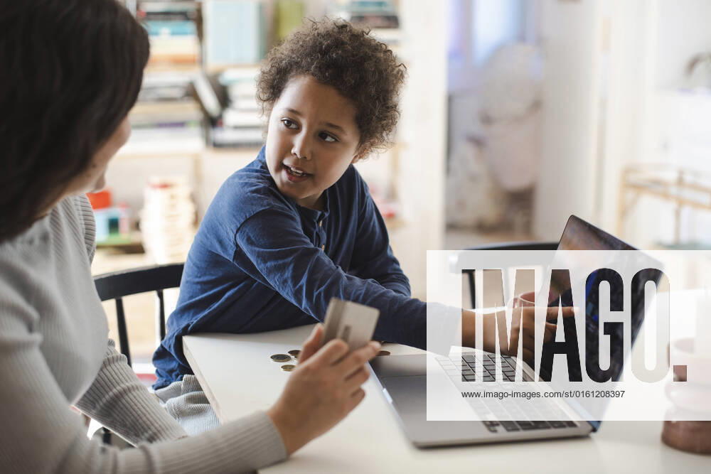 Son pointing at laptop screen while looking at mother holding credit card Sweden, Stockholm, model released, property released