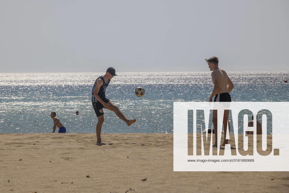 Tourism In Greece - Falassarna Beach In Crete Island Tourism in Greece - Two young men play football at the beach. The exotic beach of Falassarna at the western side of Crete island. Falasarna bay with 5 beaches with whitish sand and crystal clear transparent tropical turquoise water hosts some of the most famous beaches in Greece, which has been awarded as the best beach of Crete and voted as one of the 10 best beaches in Europe several times in the past. Local people and tourists are seen relaxing, sunbathing, tanning, swimming, doing water sports and walking. Tourism is bouncing back with reservations exceeding the pre-pandemic numbers, putting Greece and the Greek islands on high demand. Tourists travel after the Covid-19 Coronavirus pa