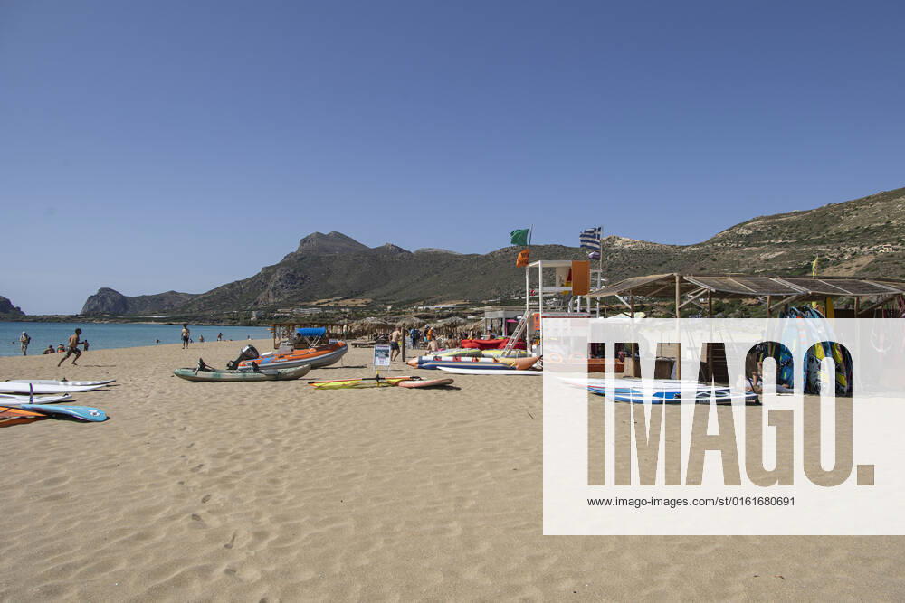 Tourism In Greece - Falassarna Beach In Crete Island Tourism in Greece - Water sports and lifeguard tower. The exotic beach of Falassarna at the western side of Crete island. Falasarna bay with 5 beaches with whitish sand and crystal clear transparent tropical turquoise water hosts some of the most famous beaches in Greece, which has been awarded as the best beach of Crete and voted as one of the 10 best beaches in Europe several times in the past. Local people and tourists are seen relaxing, sunbathing, tanning, swimming, doing water sports and walking. Tourism is bouncing back with reservations exceeding the pre-pandemic numbers, putting Greece and the Greek islands on high demand. Tourists travel after the Covid-19 Coronavirus pandemic.