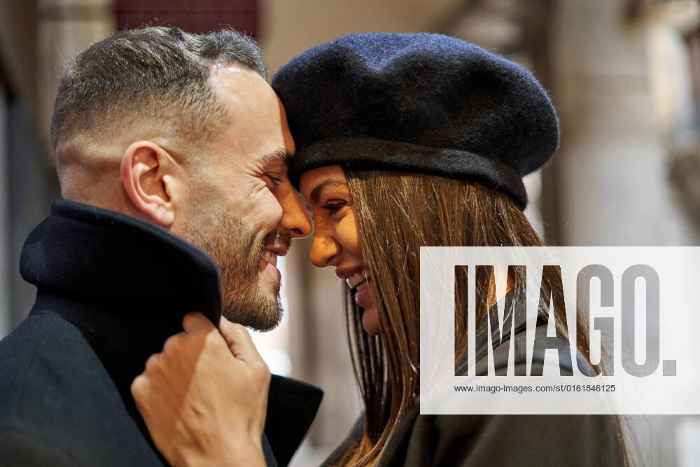 Positive couple in outerwear caressing while standing looking at each other on pathway of street near building during romantic date in city on autumn day AdalbertoRodriguez_CheerfulStylishCouple_00029.jpg