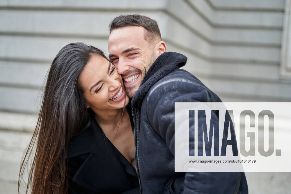 Side view of positive couple in outerwear caressing while standing on the street near building during romantic date in city on autumn day AdalbertoRodriguez_CheerfulStylishCouple_00042.jpg