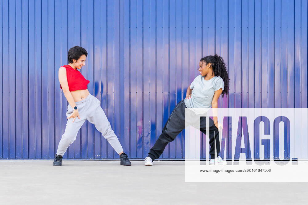 Full body side view of multiracial young female friends dancing on street near blue wall in city DavidMunoz_CarlaAndNicoleFiraDance_35.jpg