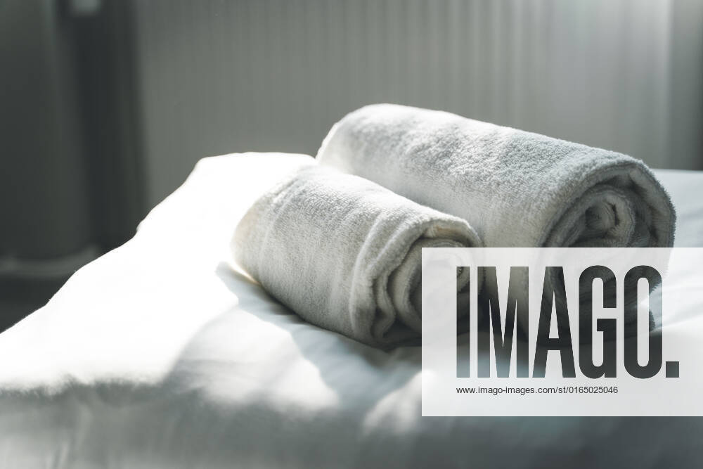 Weiße, gerollte, saubere Handtücher auf dem Hotelbett