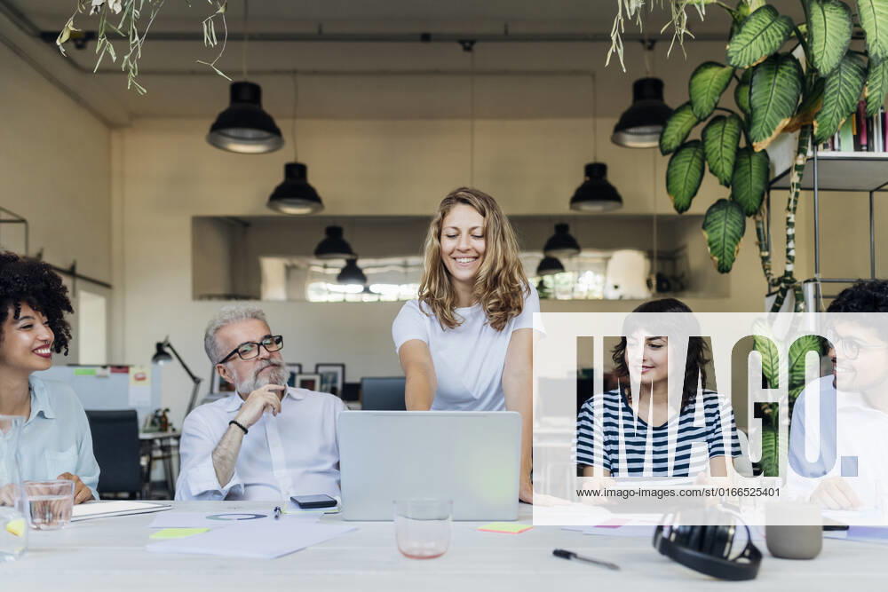Smiling businesswoman planning strategy on laptop with coworkers in office model released, Symbolfoto property released, MEUF07084