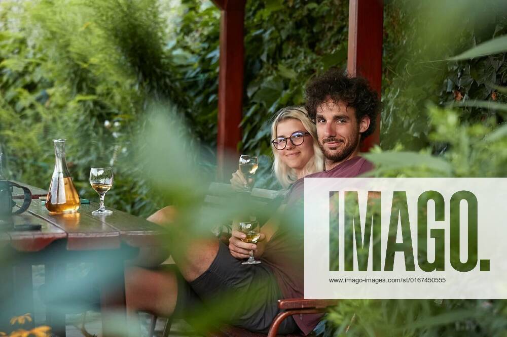 Drinking wine on a summer evening, Drinking wine, couple sitting on an outdoor terrace, shot through brances of a green bush in the forground, Drinking wine, couple sitting on an outdoor terrace, shot through brances of a green bush in the forground model released, Symbolfoto , 07.10.2021,
