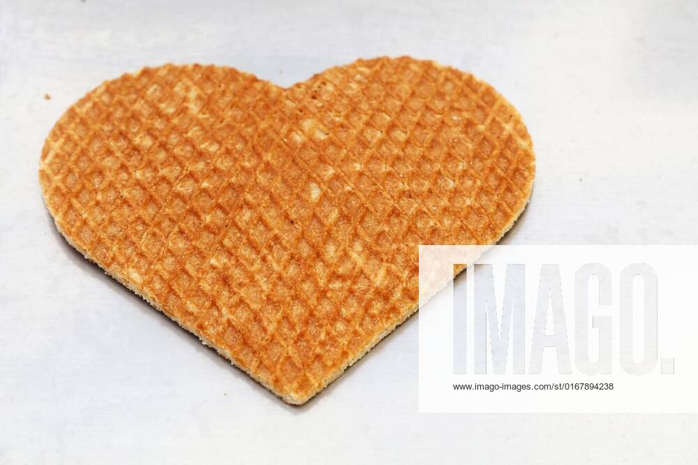 Heart shaped Dutch stroopwafel waffle on white, Close up one heart shaped traditional sweet Dutch stroopwafel (syrup waffle) cookie on white baking paper, high angle view, Close up one heart shaped traditional sweet Dutch stroopwafel (syrup waffle) cookie on white baking paper, high angle view, 28.01.2022,