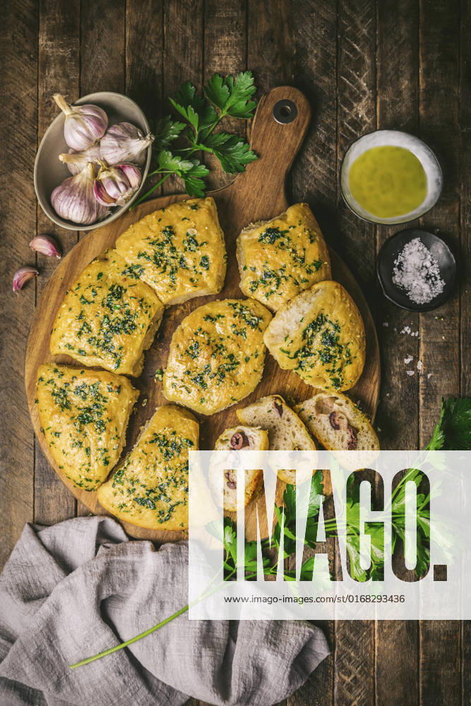IMAGO Creative, Food, Brot, Knoblauchbrot Overhead of focaccia bread with garlic and olives on a wooden board with raw garlic, parsley and olive oil Overhead of focaccia bread with garlic and olives on a wooden board with raw garlic, parsley and olive oil