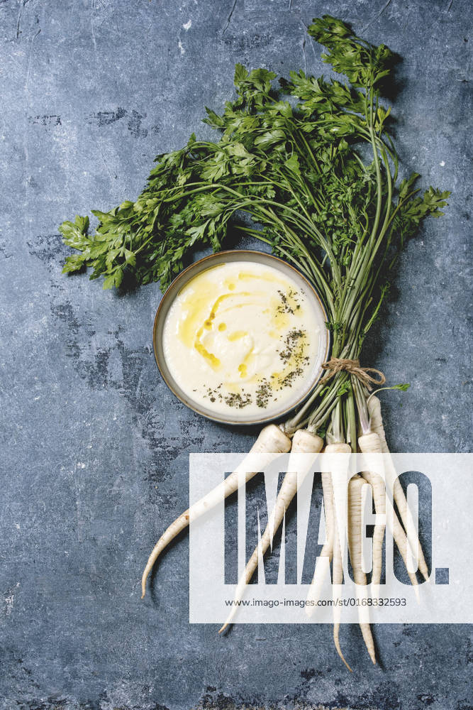 Parsnip soup with butter sauce Parsnip cream soup in ceramic bowl with butter sauce, bundle of fresh parsnip and herbs over blue texture background. Flat lay, space