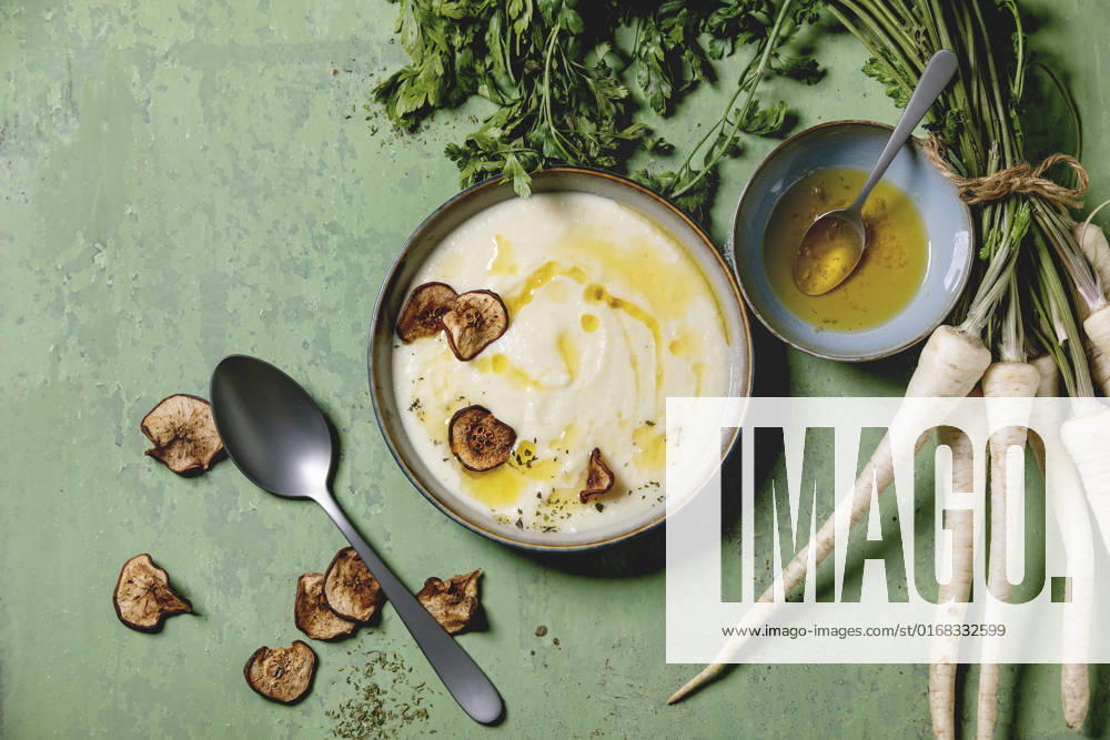 Parsnip soup with butter sauce Parsnip cream soup in ceramic bowl with sun dried pears, butter sauce, bundle of fresh parsnip and herbs over green texture background. Flat lay, space