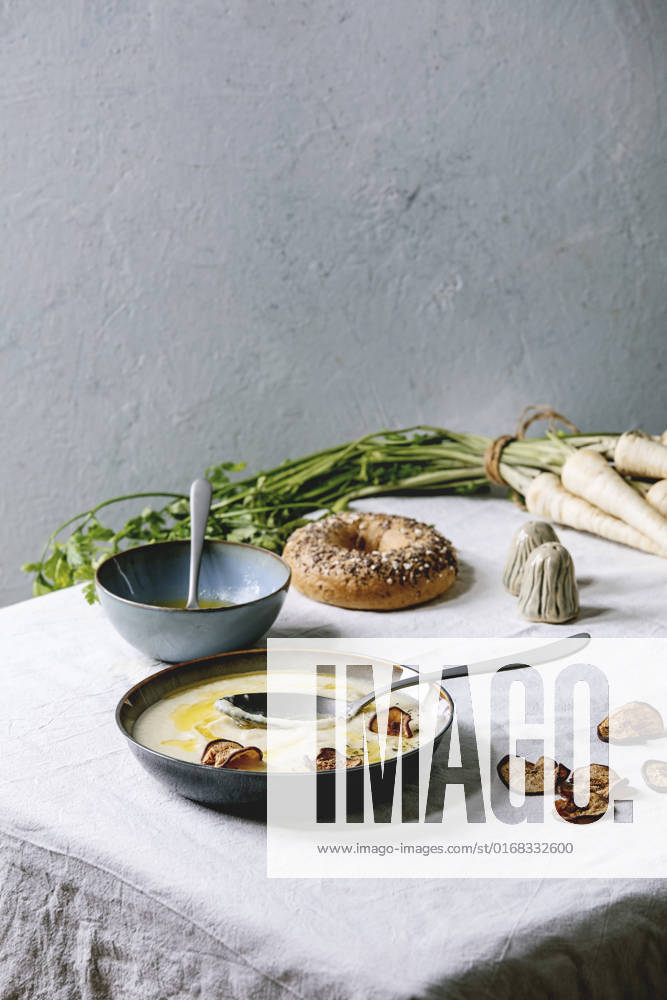 Parsnip soup with butter sauce Parsnip cream soup in ceramic bowl with butter sauce, sun dried pears, bundle of fresh parsnip, bagel bread and herbs on kitchen table with white tablecloth
