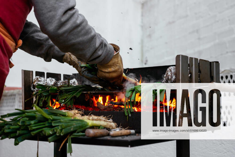 Crop anonymous person in protective gloves grilling traditional Catalonian calcots on hot barbecue grid with foil while standing on terrace, Model released AidaMartinez_BBQCalcots_11