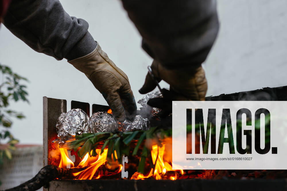 Crop anonymous person in protective gloves grilling traditional Catalonian calcots on hot barbecue grid with foil while standing on terrace, Model released AidaMartinez_BBQCalcots_6