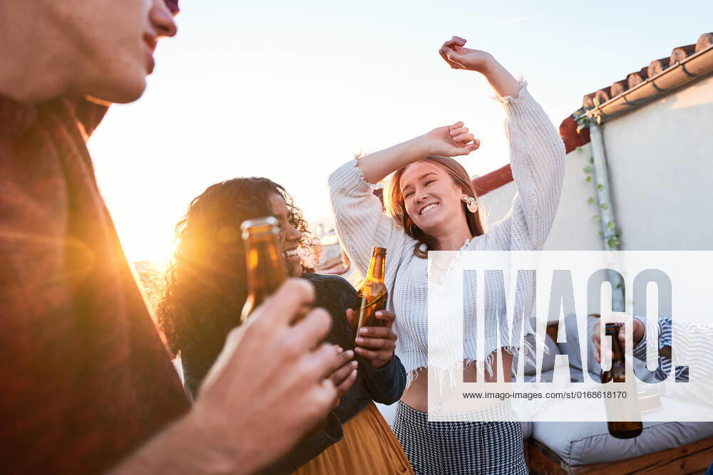 IMAGO Creative, Urban Lifestyle IMAGO Kreativ: Urbane Kultur - Sommer auf den D?chern Group of joyful young multiracial friends wearing casual clothes enjoying cold beer and dancing with arms raised together on rooftop at sunset, Model released, Property released ManuelRuiz_FlatmatesMusiciansTerrace_68