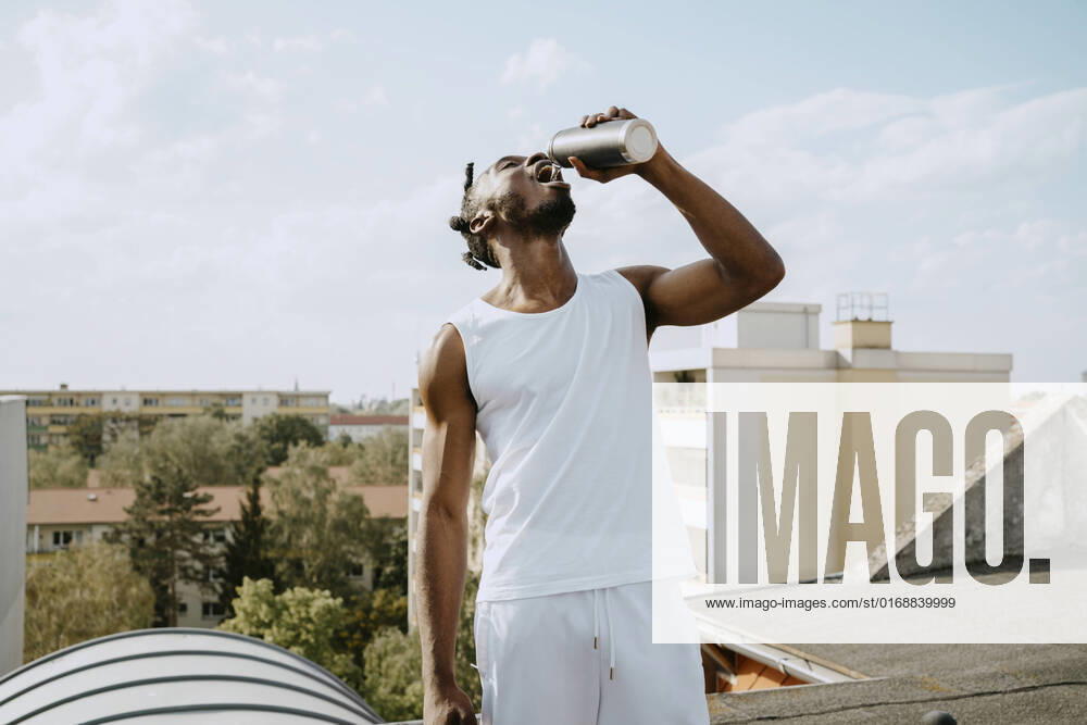 IMAGO Creative: 2022 Sport Favoriten IMAGO Creative: Menschen in Berlin Young man drinking water from bottle while standing on rooftop during sunny day Germany, Berlin, model released, property released
