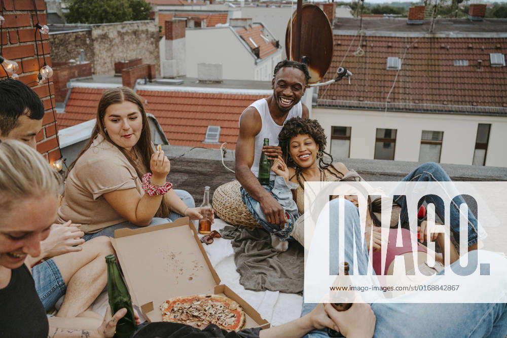 IMAGO Creative, Urban Lifestyle IMAGO Kreativ: Urbane Kultur - Sommer auf den Dächern Happy male and female friends with pizza enjoying party on rooftop Germany, Berlin, model released, property released