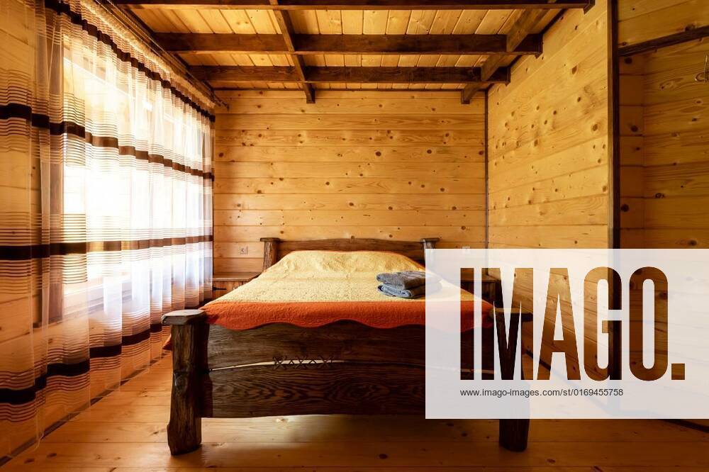 Rustic wooden bed in a cozy cottage room with a double bed, bedside table, blankets and towels., Rustic wooden bed by the window in a cozy cottage hotel room with a double bed, bedside table, blankets and towels. Interior of a wooden house. Eco friendly furniture and style concept., Rustic wooden bed by the window in a cozy cottage hotel room with a double bed, bedside table, blankets and towels. Interior of a wooden house. Eco friendly furniture and style concept., 30.05.2022,