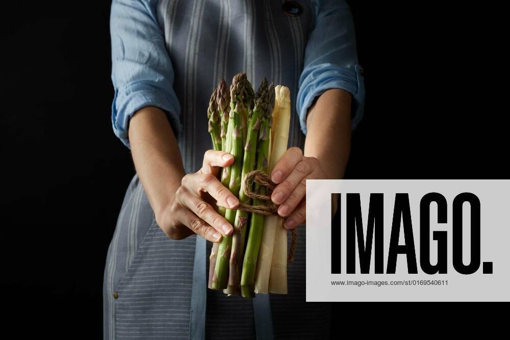 IMAGO Creative: Food, Spargel Faceless cook with raw asparagus, Crop anonymous female holding fresh heap of fresh uncooked raw and white asparagus while standing against black background in studio, Crop anonymous female holding fresh heap of fresh uncooked raw and white asparagus while standing against black background in studio, 30.06.2022,