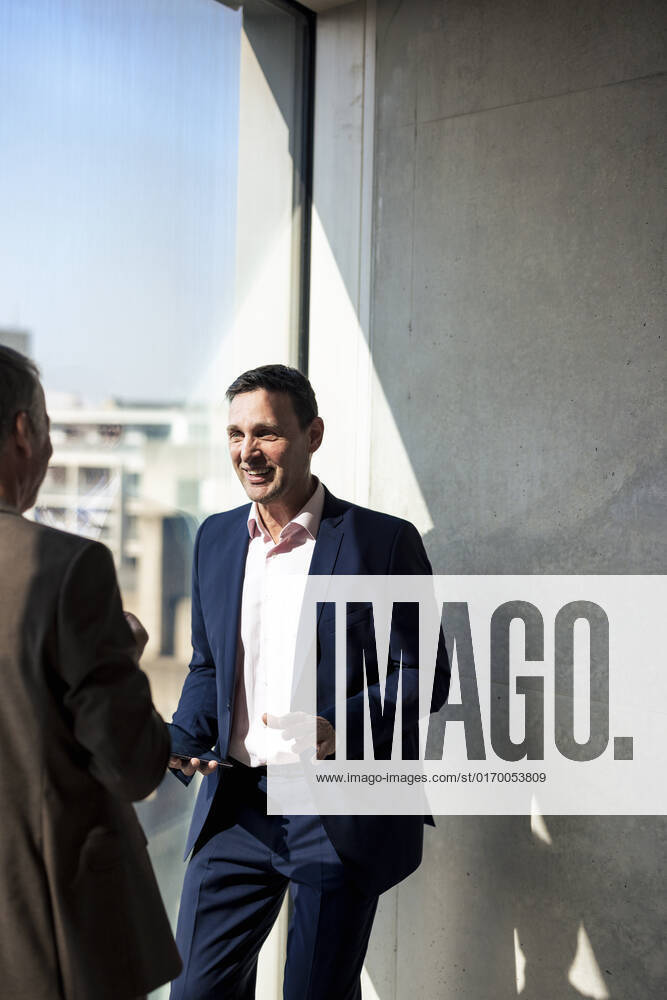 Smiling businessman planning strategy with colleague by window in office model released, Symbolfoto property released, JOSEF12710