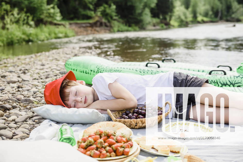 Boy sleeping on picnic blanket by cherry basket at riverbank model released, Symbolfoto, VBUF00138