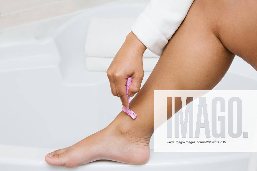 Crop unrecognizable female in bathrobe shaving legs with razor while doing skin care routine in bathroom, Model released AngelaRober_AnnyPersonalCare_28