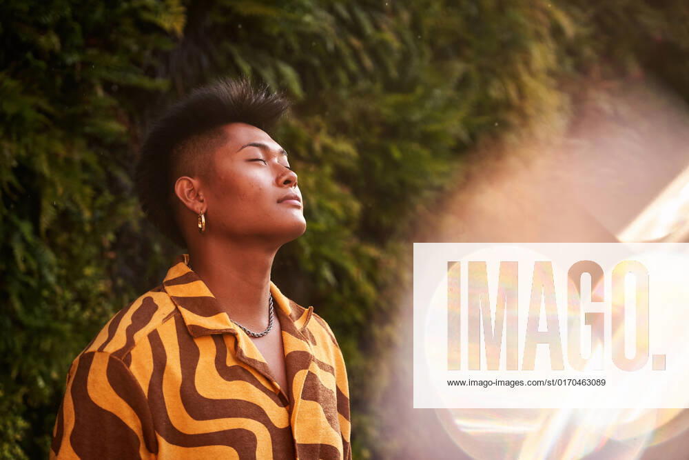 Dreamy young Filipino non binary man wearing cool shirt with earring standing with eyes closed in green garden ManuelRuiz_ID927_33966_028