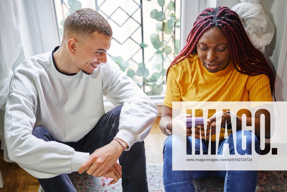 Multiracial couple looking at the mobile sitting on the floor at home Valencia, Valencian Community, Spain CR_VFKDPR221019-1058219-01 ,model released, Symbolfoto