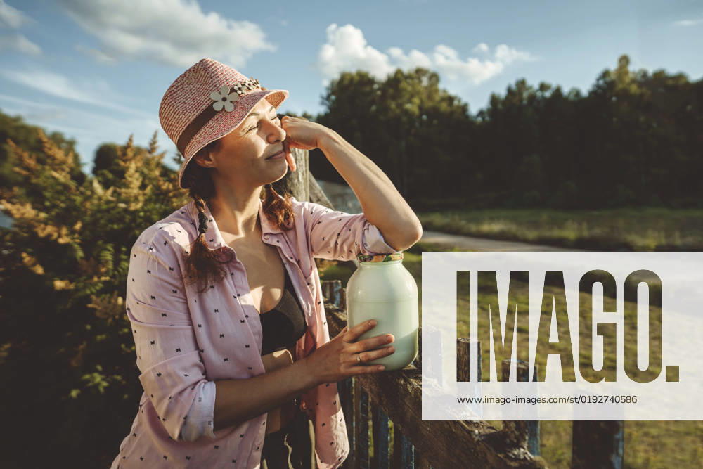 Woman standing with jar full of milk by fence on sunny day model released, Symbolfoto property released, IEF00158