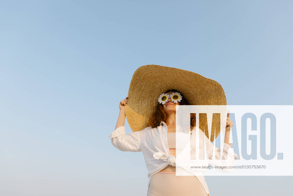 Smiling woman wearing sunflower sunglasses and oversized straw hat on sunny day model released, Symbolfoto, TYF00431