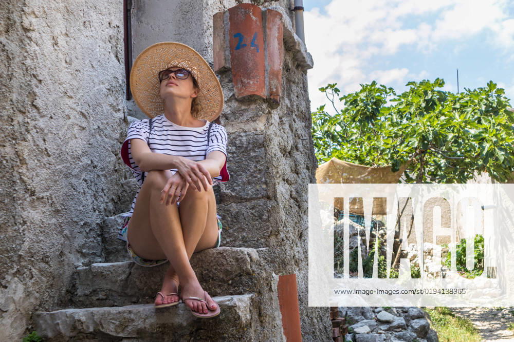 IMAGO Creative, Jahreszeit Sommer, Hitze IMAGO Creative, Sommer, Schatten-Plätze bei Hitze Beautiful female tourist wearing big straw sun hat and shorts sitting and relaxing on old stone house stairs during summer travel on Mediterranean cost on hot summer day Beautiful female tourist wearing big straw sun hat and shorts sitting and relaxing on old stone house stairs during summer travel Mediterranean costal village on hot summer day.