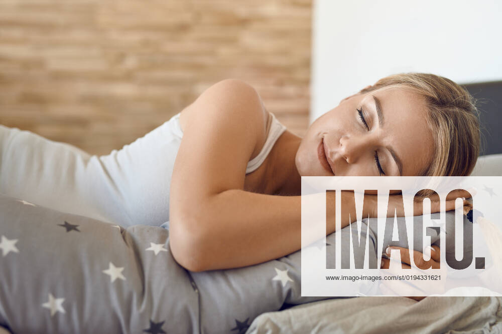 Hübsche Frau mit Schwangerschaftskissen Pretty young pregnant woman sleeping using a special support cushion running the length of her body in a close up view with a peaceful serene expression
