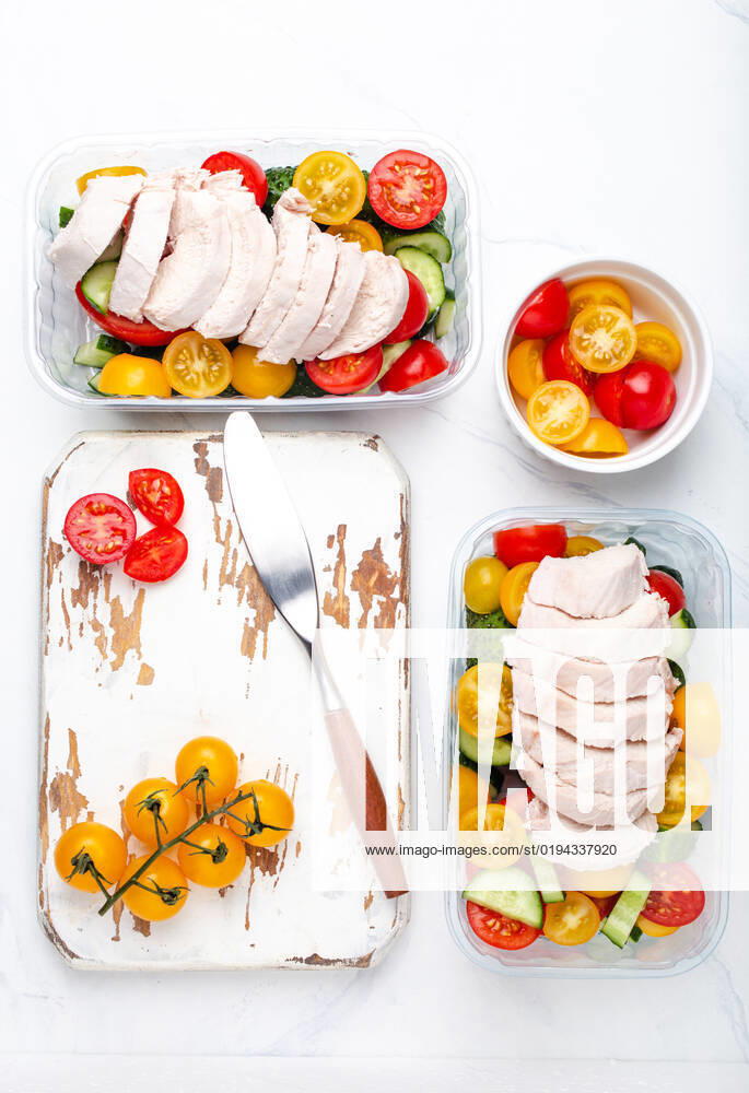 Meal prep lunch boxes containers with chicken and salad top view Healthy meal prep for lunch, diet boiled chicken fillet with vegetables salad in lunch boxes containers top view on white marble kitchen table background with knife and cutting board