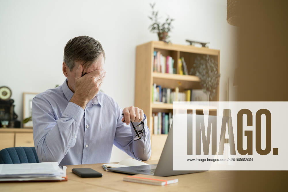 Stressed senior businessman with hand on face doing home office