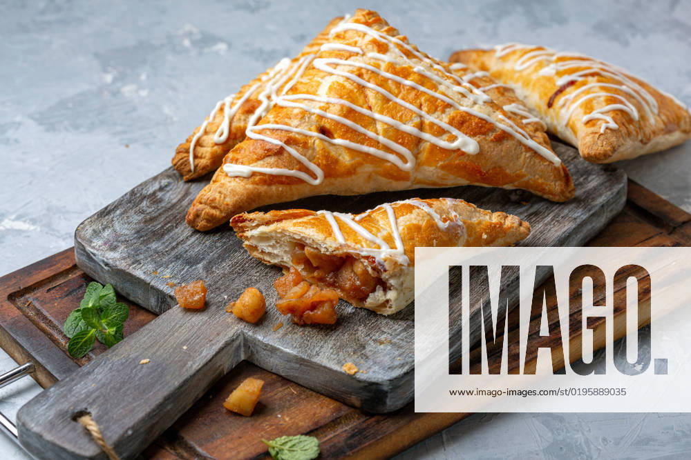 IMAGO Creative, Food, Gebäck, Apfeltaschen Puff pastry turns with apple filling. Puff pastry turnovers filled with apples on a wooden serving board, selective focus. Homemade food concept.