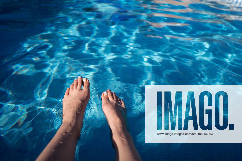 From above anonymous barefoot female tourist wetting legs in blue water of clean pool on summer day on resort, Model released JuanAlbertoRuiz_ID10616_321593_004