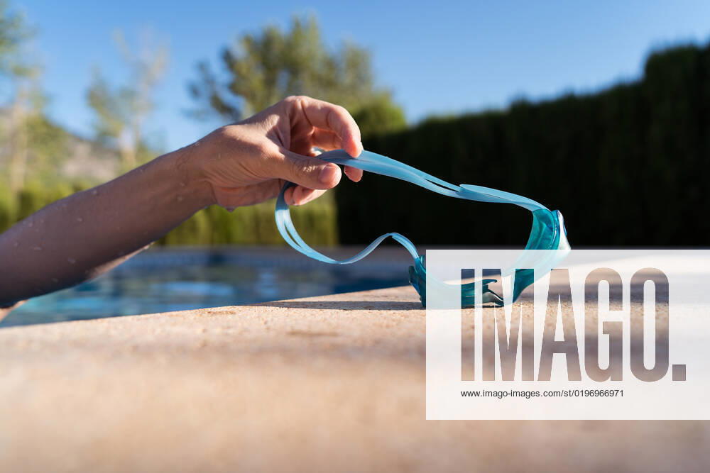 Crop anonymous man standing in water of clean pool and taking off goggles after swim on cloudless weekend day on resort, Model released JuanAlbertoRuiz_ID10616_321601_008