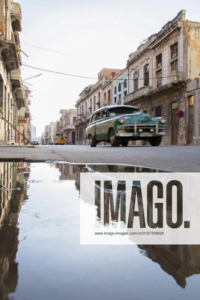 Cuba, Havana, Vintage car driving past street puddle, MMPF00551