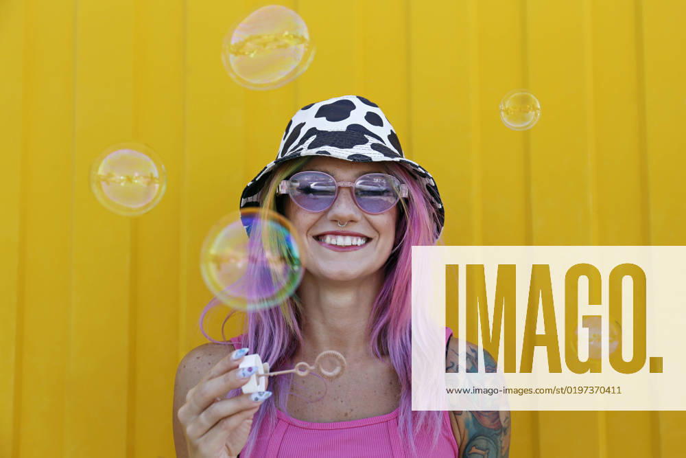 Happy woman holding bubble wand in front of yellow wall model released, Symbolfoto property released, SYEF00145