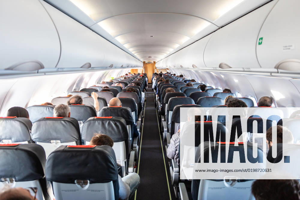 Interior of commercial airplane with passengers on their seats during flight. Interior of commercial airplane with unrecognizable passengers on their seats during flight shot from the rear of airplane.