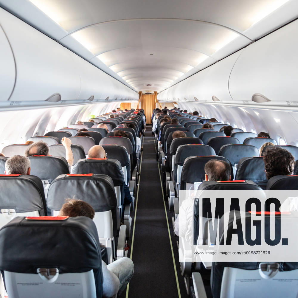 Interior of commercial airplane with passengers on their seats during flight. Interior of commercial airplane with unrecognizable passengers on their seats during flight shot from the rear of airplane.
