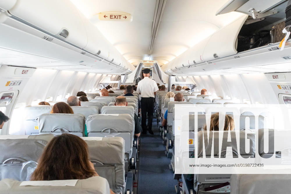 Interior of commercial airplane with passengers on their seats during flight. Interior of commercial airplane with unrecognizable passengers on their seats during flight. Steward in blue white uniform walking the aisle of commercial airplane.