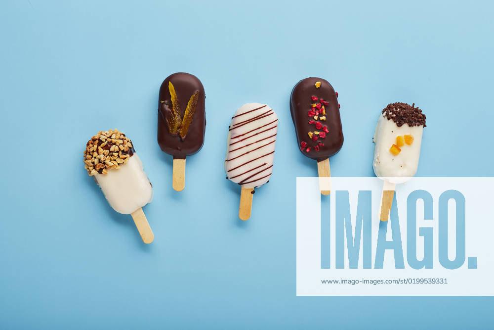 Mousse dessert with fruit flavors in the form of popsicle ice cream on blue background. Mousse dessert with fruit flavors in the form of popsicle ice cream covered with white and dark chocolate on a blue background.