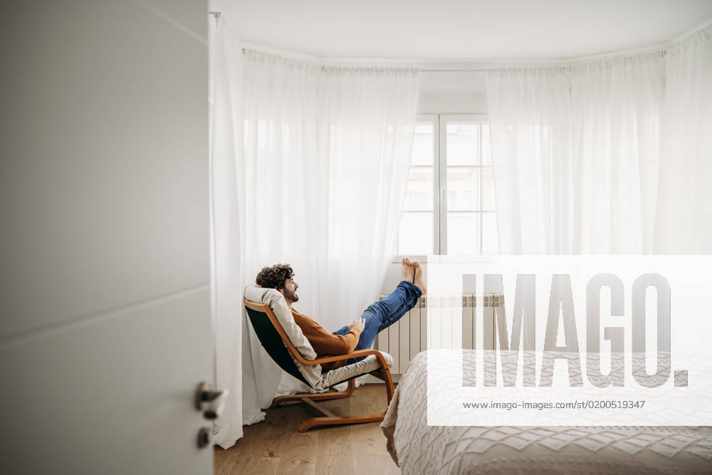 Young man relaxing on armchair in bedroom at home model released, Symbolfoto property released, EBBF07521