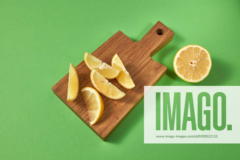 Half and slices of fresh tropical yellow lemon on a wooden cutting brown board. View from above. Citrus fruits on a green background with place for text. Citrus fruits on a green background with place for text. Top view of slices of natural yellow lemon for preparing homemade lemonade on a wooden board on green.