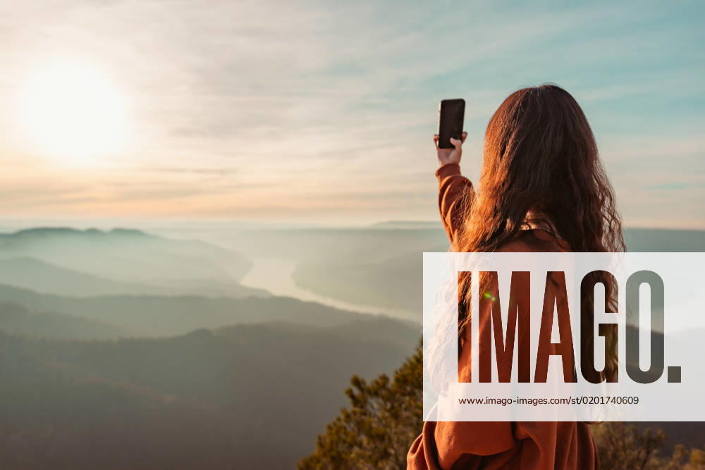 Anonymous female traveler in casual sweater taking picture of amazing landscape with mountains and sunset sky on smartphone during vacation in Almatret, Model released HiCarles_ID12666_384789_008