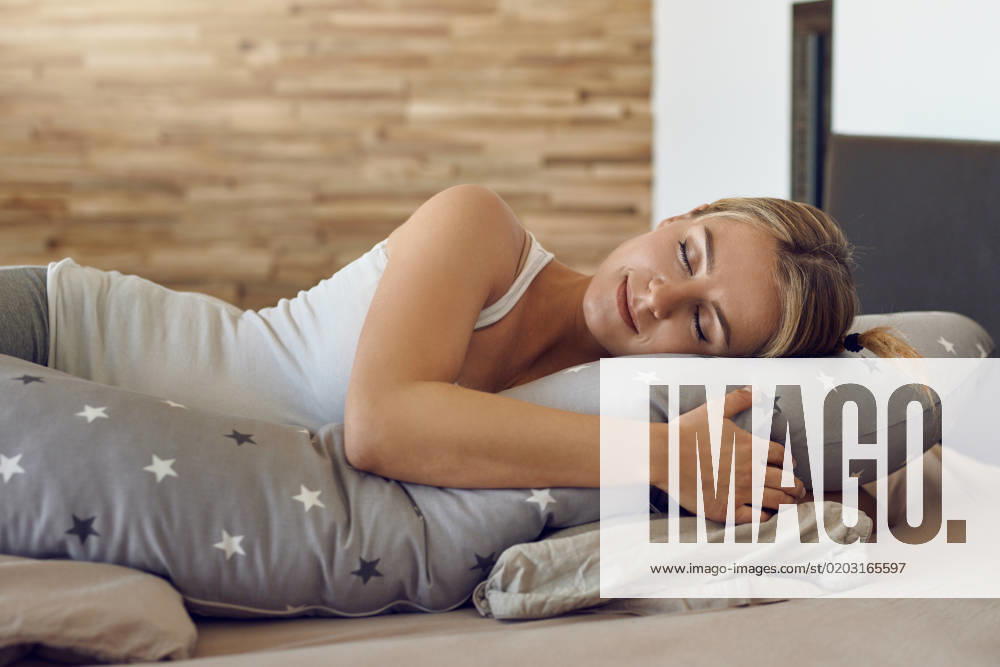 Hübsche Frau mit Schwangerschaftskissen Pretty young pregnant woman sleeping using a special support cushion running the length of her body in a close up view with a peaceful serene expression
