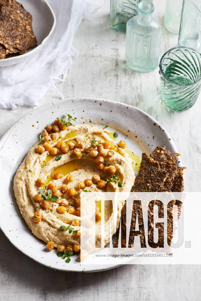 IMAGO Creative, Food, Hummus Top view of delicious hummus with chickpeas seeds and olive oil served on plate with crispy healthy crackers on table in kitchen GeorgiaGold_ID12873_391219_002