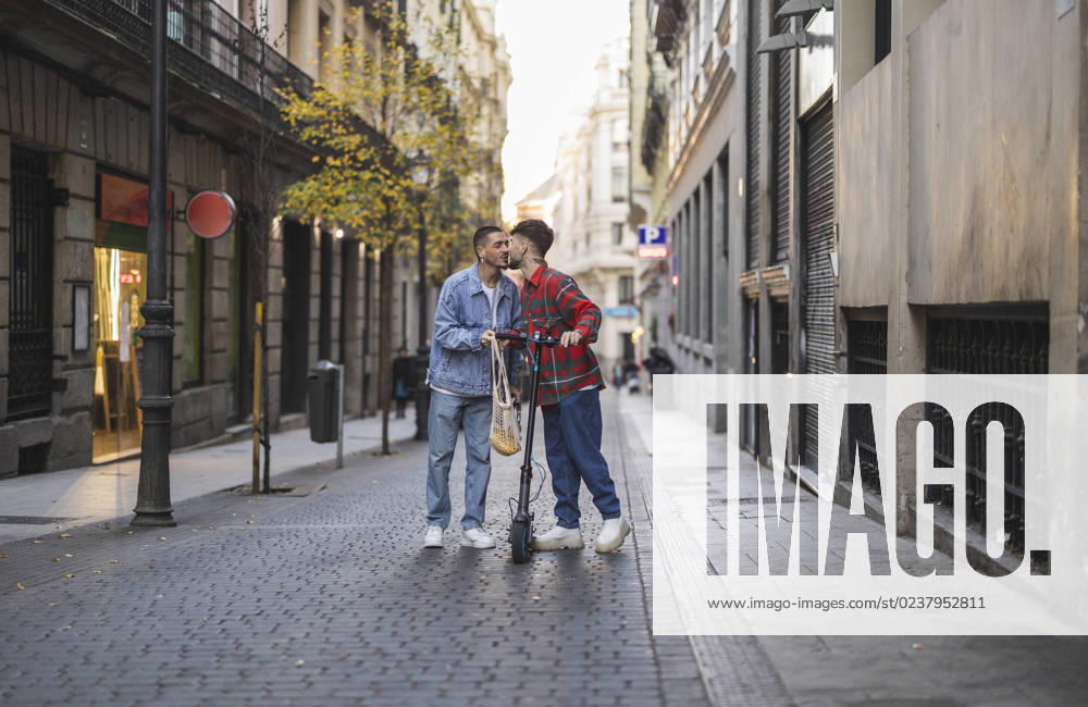 IMAGO Creative, Urban Lifestyle Happy gay couple kissing with electric push scooter amidst buildings model released, Symbolfoto property released, JCCMF09174